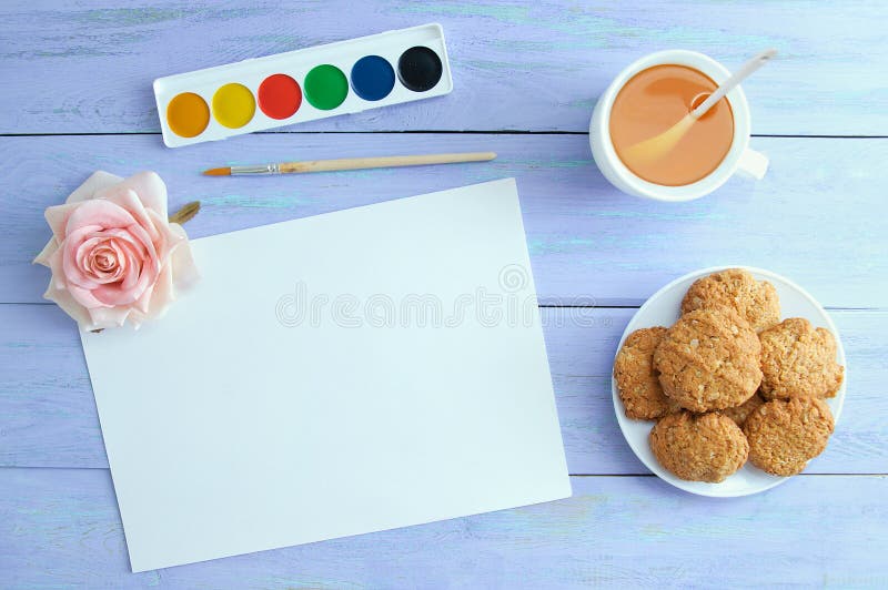 Hoja de papel blanca, acuarelas, té verde en una taza y galletas imagen de archivo Hoja de papel blanca, acuarelas, té verde en una taza y galletas imagen de archivo