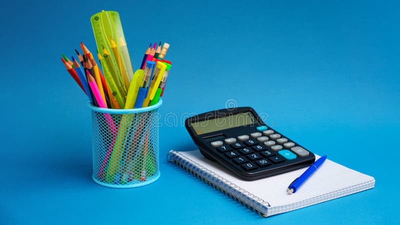 Holder with pens and pencils and notebook with calculator on blue background. stock photo.