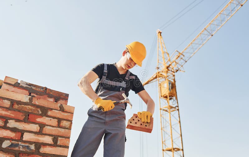 Holding Brick and Using Hammer. Construction Worker in Uniform and