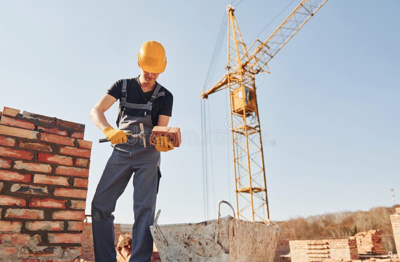Holding Brick and Using Hammer. Construction Worker in Uniform and