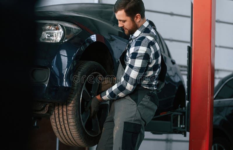 Holding and Changing New Tire. Man in Uniform is Working in the Auto
