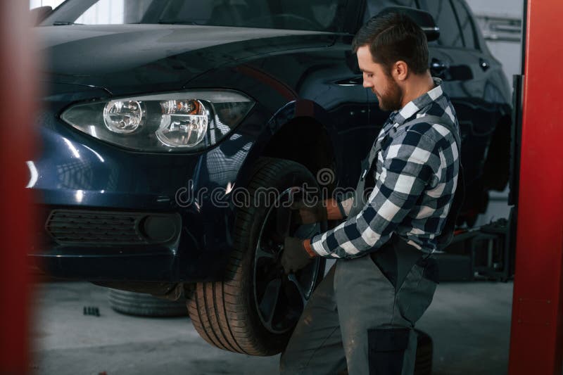 Holding and Changing New Tire. Man in Uniform is Working in the Auto