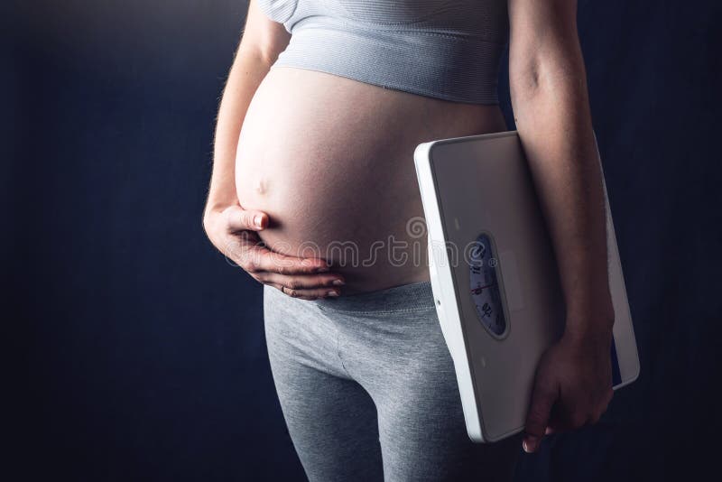 Pregnant woman holding scales and weigh keeping one hand on a belly. The concept of weight loss and control during pregnancy. Pregnant woman holding scales and weigh keeping one hand on a belly. The concept of weight loss and control during pregnancy