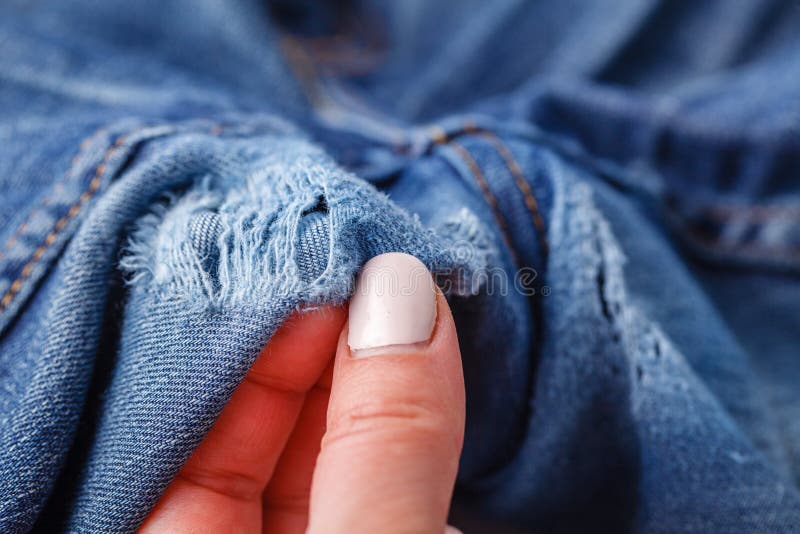 Hole and Threads on Denim Jeans. Ripped Destroyed Torn Blue Jeans