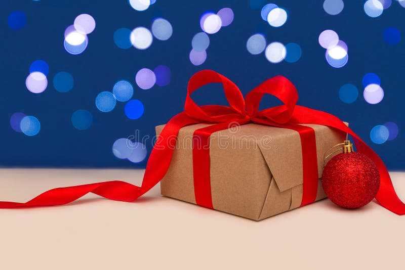 Holiday concept. Christmas gift box with red bow and christmas red ball on blue bokeh background. Holiday greeting card. Copy stock image Holiday concept. Christmas gift box with red bow and christmas red ball on blue bokeh background. Holiday greeting card. Copy stock image