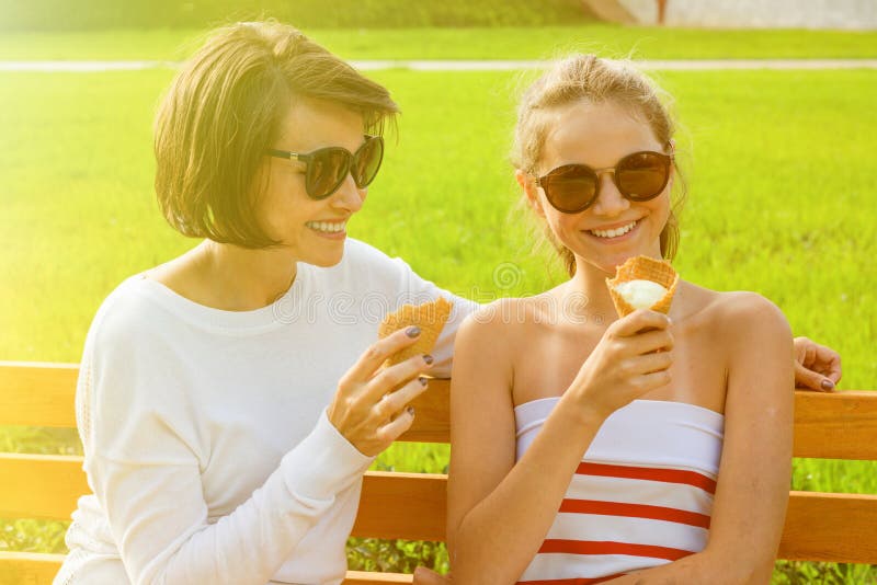 Happy young mother and cute daughter of a teenager in a city park eating ice cream, talking and laughing stock photo Happy young mother and cute daughter of a teenager in a city park eating ice cream, talking and laughing stock photo