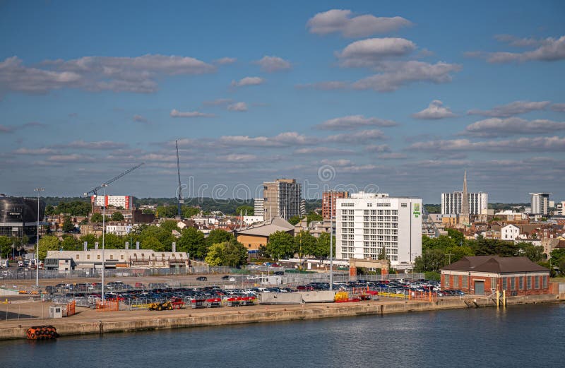 Southampton, England, UK - July 7, 2022: Harbor scenery. White Holiday Inn hotel towers over dock at port under blue cloudscape. Pire os St Michael the Archangel church on right, Westquay on left. Southampton, England, UK - July 7, 2022: Harbor scenery. White Holiday Inn hotel towers over dock at port under blue cloudscape. Pire os St Michael the Archangel church on right, Westquay on left