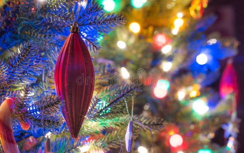 Holiday season, christmas tree decorations glow under luminous and vivid, colorful lights on a small faux indoor tree. Globes, ball.