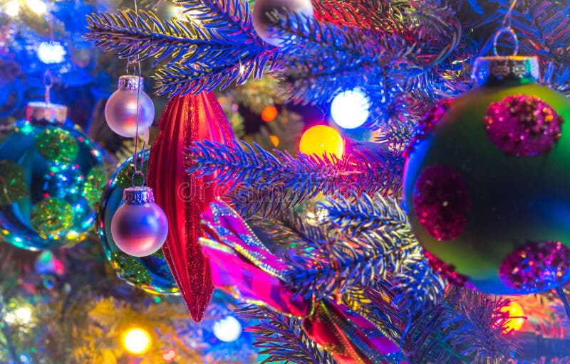 Holiday season, Christmas tree decorations glow under luminous and vivid, colorful lights on a small faux indoor tree.