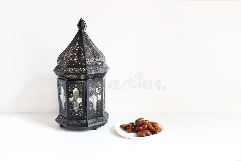 Holiday still life composition. Plate with date fruits and ornamental dark Moroccan, Arabic lantern on the white table