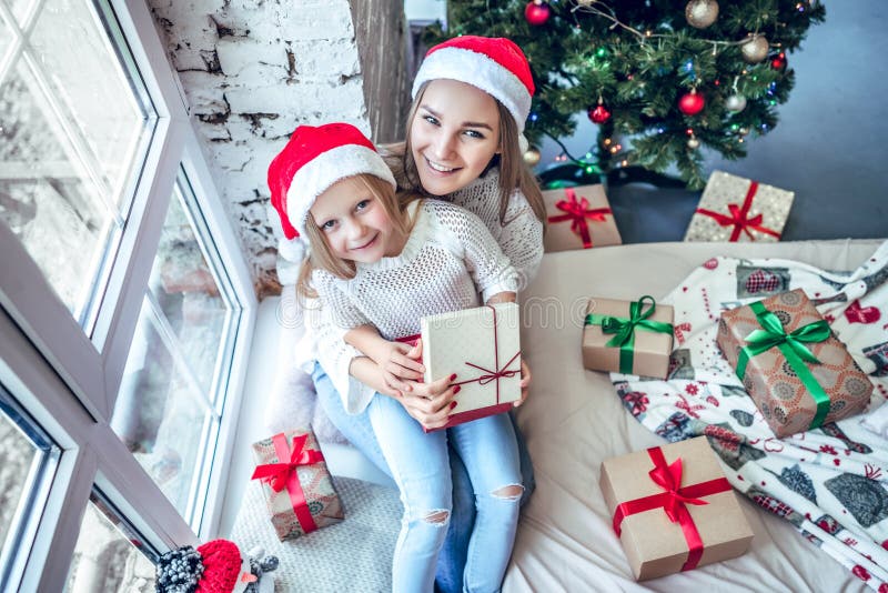 Happy mother and little girl in santa helper hats with gift box over living room and christmas tree background royalty free stock image Happy mother and little girl in santa helper hats with gift box over living room and christmas tree background royalty free stock image