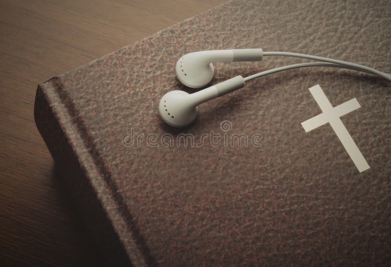 Holy Bible with a resting pair of earbuds over it. The word of God through hearing.