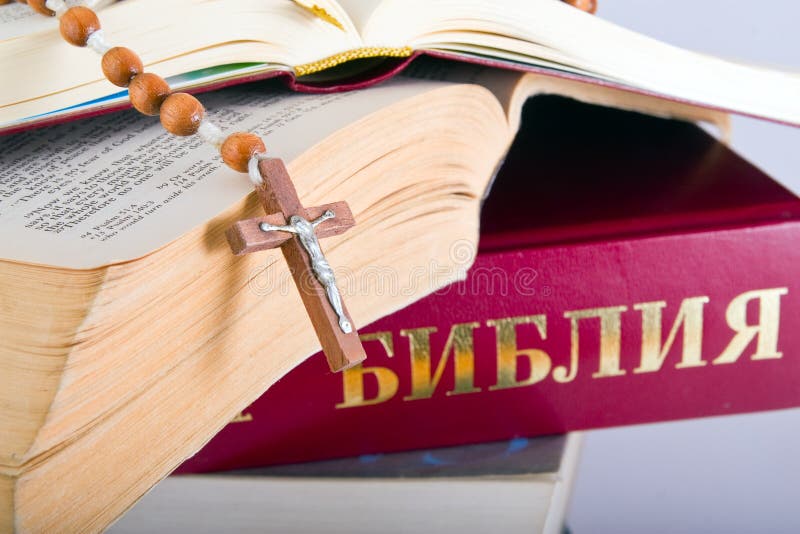 Holy Bible with rosary on pile of old books