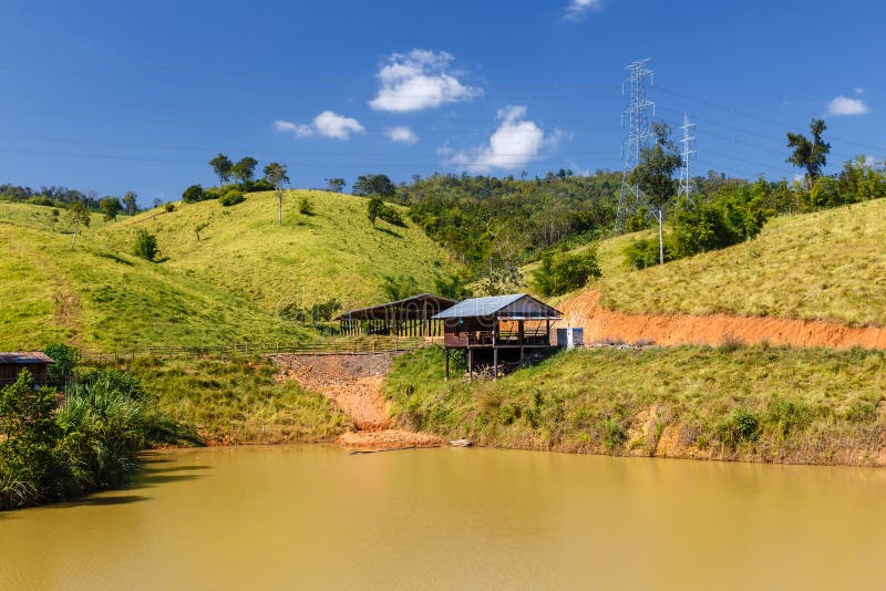 Holzhaus durch den Teich und die Stromleitung im Hintergrund, Laos stockfotografie Holzhaus durch den Teich und die Stromleitung im Hintergrund, Laos stockfotografie
