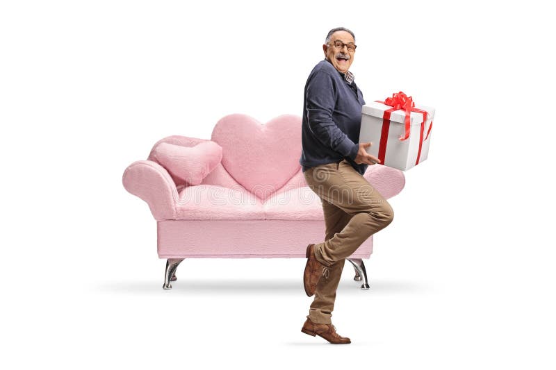 Hombre adulto exaltado sostiene una caja de regalo frente a un sofá rosa imagenes de archivo