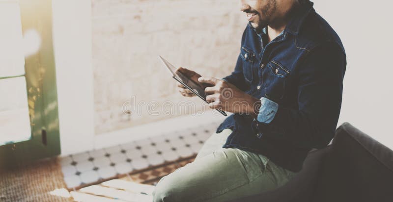 Hombre africano barbudo joven que usa la tableta mientras que se sienta en el sofá en su oficina coworking moderna Concepto de ge foto de archivo libre de regalías Hombre africano barbudo joven que usa la tableta mientras que se sienta en el sofá en su oficina coworking moderna Concepto de ge foto de archivo libre de regalías