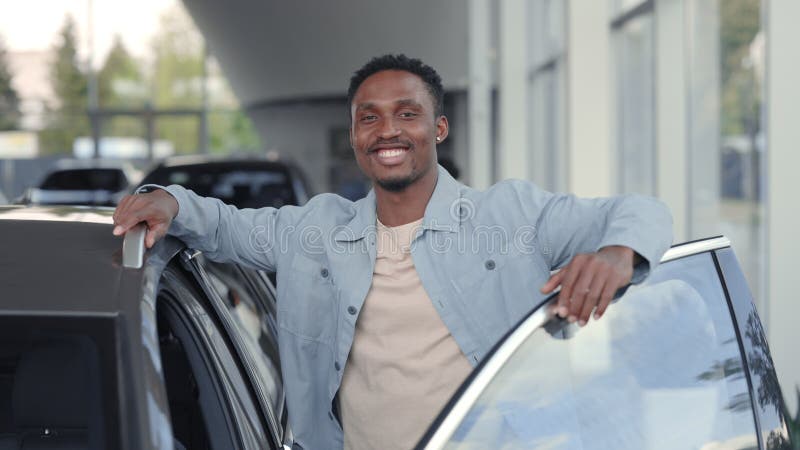 Hombre africano feliz de pie en el concesionario cerca de coche de lujo