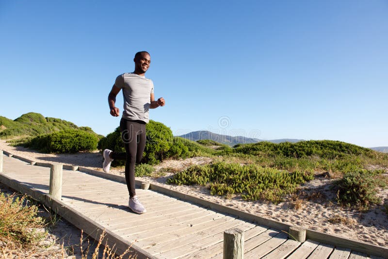 Hombre africano joven sano que corre en paseo marítimo en la playa fotos de archivo Hombre africano joven sano que corre en paseo marítimo en la playa fotos de archivo