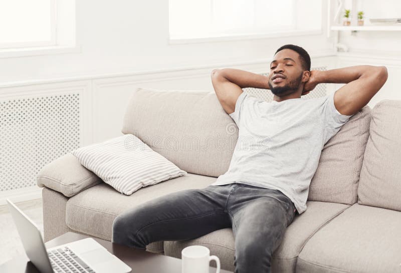 Hombre afroamericano joven hermoso que se relaja en el sofá en casa imagen de archivo Hombre afroamericano joven hermoso que se relaja en el sofá en casa imagen de archivo