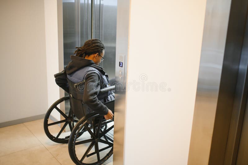 Hombre afroamericano usando ascensor en silla de ruedas fotografía de archivo