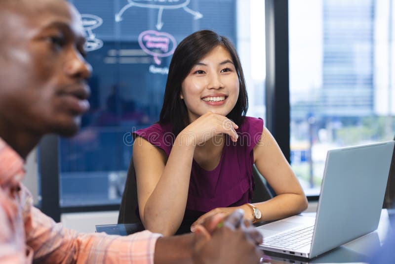 African American man and Asian woman working together in a modern business office, both looking happy. She has long black hair, he wears glasses, and they are using a laptop, unaltered. African American man and Asian woman working together in a modern business office, both looking happy. She has long black hair, he wears glasses, and they are using a laptop, unaltered.