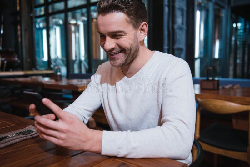 Hombre agradable feliz que mira la pantalla de su smartphone foto de archivo Hombre agradable feliz que mira la pantalla de su smartphone foto de archivo