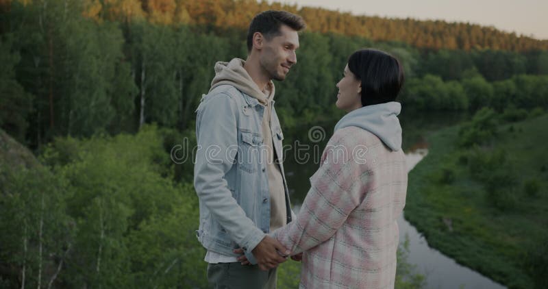 Hombre amante expresando amor a la mujer y luego viendo el espectacular paisaje de bosque y río parado en la montaña juntos