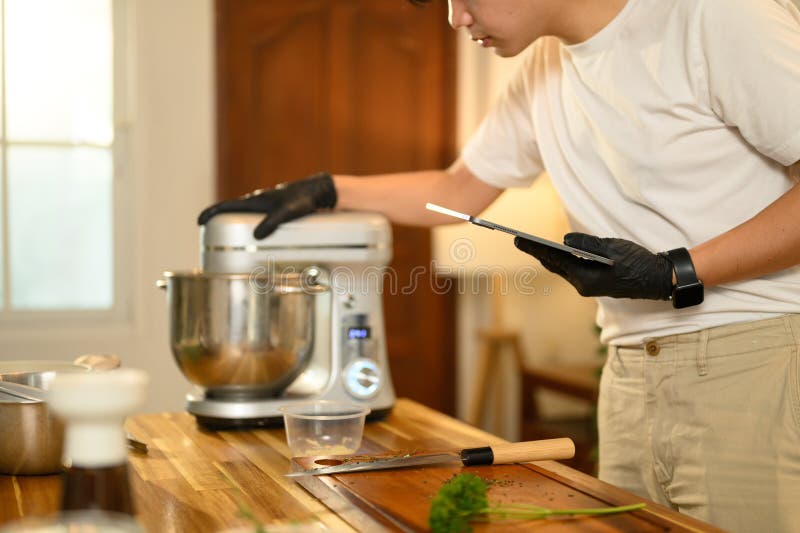 Hombre asiático en la cocina revisando una receta en una tableta digital mientras preparaba crema batida imagen de archivo
