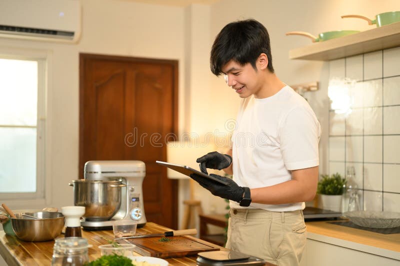 Hombre asiático en la cocina revisando una receta en una tableta digital mientras preparaba crema batida fotografía de archivo libre de regalías