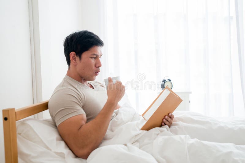 Hombre asiático que bebe una taza de café o de desayuno en cama fotografía de archivo Hombre asiático que bebe una taza de café o de desayuno en cama fotografía de archivo