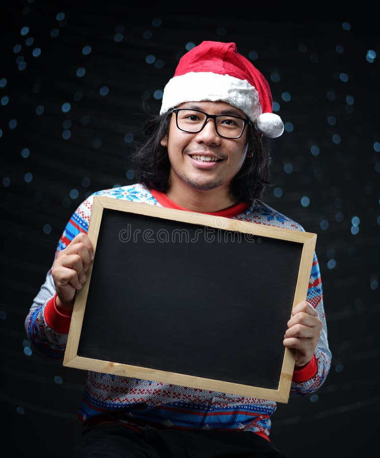 Hombre asiático que lleva Santa Hat y el suéter de la Navidad que sostienen Blackb fotos de archivo Hombre asiático que lleva Santa Hat y el suéter de la Navidad que sostienen Blackb fotos de archivo
