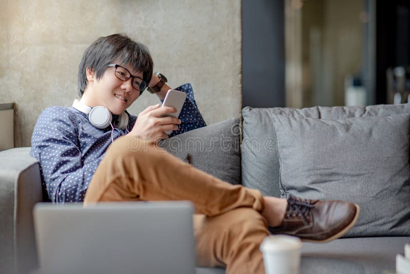 Hombre asiático que usa smartphone en el sofá fotos de archivo Hombre asiático que usa smartphone en el sofá fotos de archivo