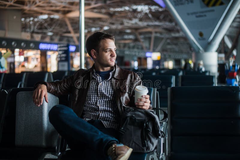 Hombre atractivo joven en el aeropuerto con su maleta y café del bolso imágenes de archivo libres de regalías Hombre atractivo joven en el aeropuerto con su maleta y café del bolso imágenes de archivo libres de regalías