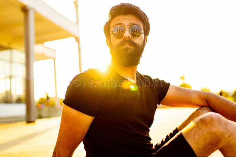 Hombre barbudo con camiseta de algodón negro calentando al aire libre en el parque de verano al atardecer luz de oro.