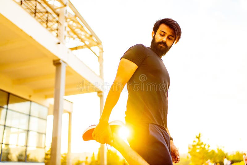 Hombre barbudo con camiseta de algodón negro calentando al aire libre en el parque de verano al atardecer luz de oro imagenes de archivo