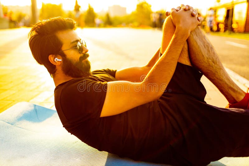 Hombre barbudo con camiseta de algodón negro calentando al aire libre en el parque de verano al atardecer luz de oro fotografía de archivo