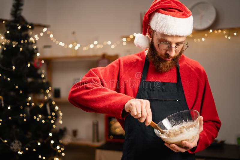 Hombre barbudo con sombrero de santa para hacer masa para galletas de navidad tradicionales cocinando en una cocina acogedora. espacio de copia