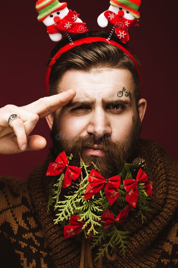 Hombre barbudo divertido en una imagen del ` s del Año Nuevo como Santa Claus con las decoraciones en su barba Banquete de la Nav imagenes de archivo Hombre barbudo divertido en una imagen del ` s del Año Nuevo como Santa Claus con las decoraciones en su barba Banquete de la Nav imagenes de archivo