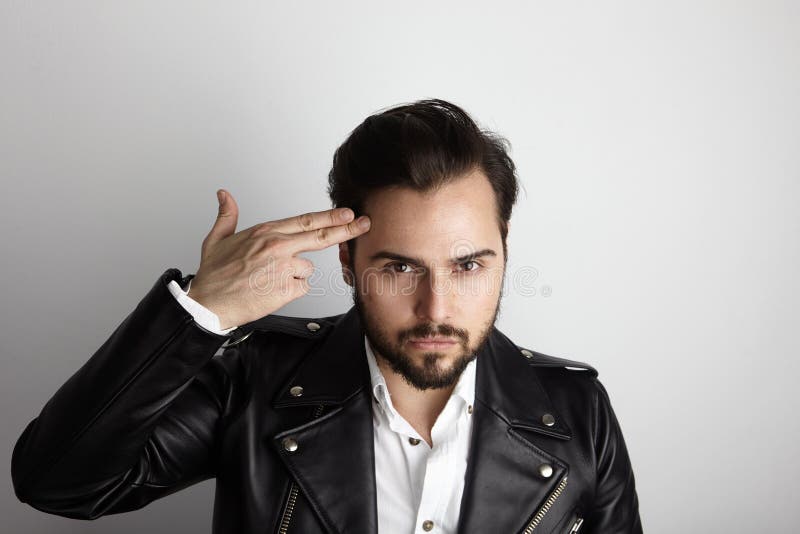 Hombre barbudo joven hermoso que lleva la cabeza elegante de la mano del tiro de la chaqueta de cuero del negro de la camisa Bell foto de archivo Hombre barbudo joven hermoso que lleva la cabeza elegante de la mano del tiro de la chaqueta de cuero del negro de la camisa Bell foto de archivo