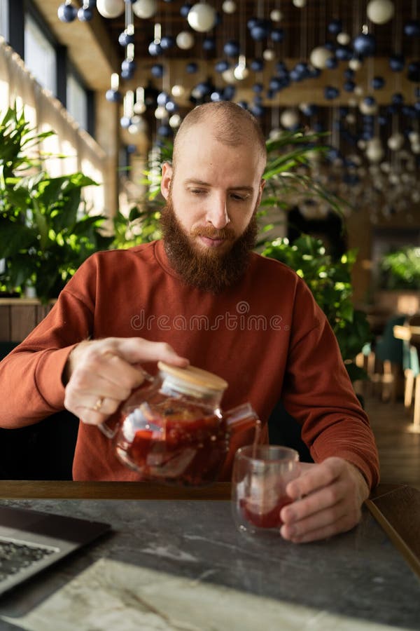 Hombre barbudo vertiendo té de hierbas en un acogedor café imagen de archivo