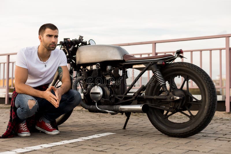 Hombre brutal cerca de su moto de la aduana del corredor del café foto de archivo libre de regalías Hombre brutal cerca de su moto de la aduana del corredor del café foto de archivo libre de regalías