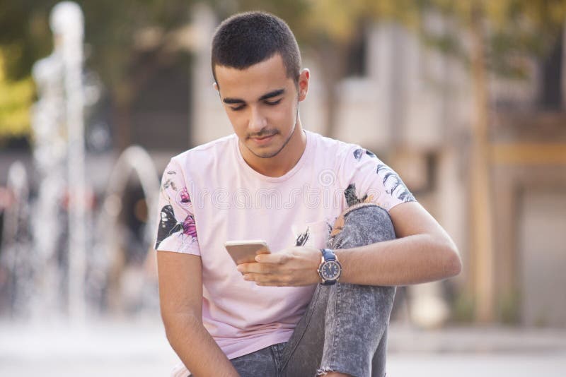 Hombre casual joven que camina y que lee mensajes en el phon elegante foto de archivo libre de regalías Hombre casual joven que camina y que lee mensajes en el phon elegante foto de archivo libre de regalías