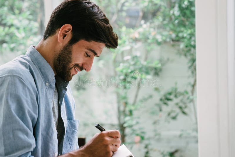 Hombre caucásico con bigote y barba escribiendo en un cuaderno foto de archivo