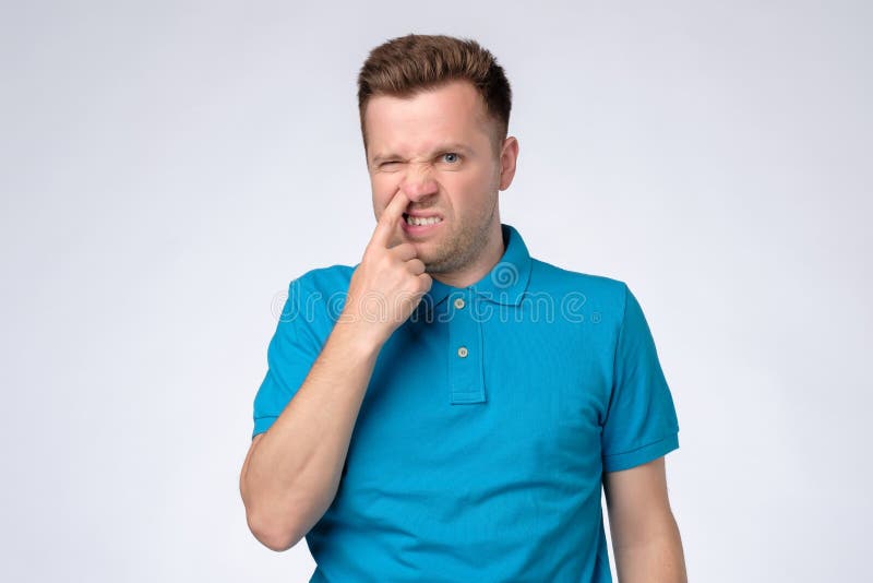 Hombre caucásico joven en la camisa azul que escoge en su nariz foto de archivo libre de regalías Hombre caucásico joven en la camisa azul que escoge en su nariz foto de archivo libre de regalías
