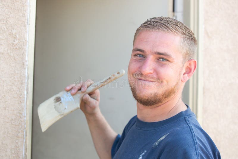Hombre caucásico joven que sonríe como él está pintando la casa imagen de archivo libre de regalías Hombre caucásico joven que sonríe como él está pintando la casa imagen de archivo libre de regalías