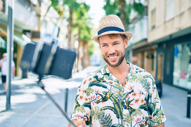 Hombre caucásico y apuesto sonriendo feliz al aire libre tomando un selfie usando palo de selfie imagen de archivo libre de regalías
