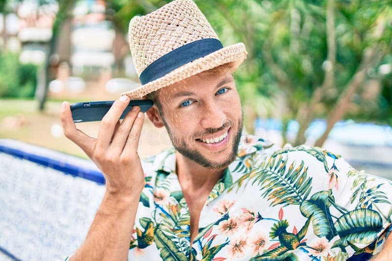 Hombre caucásico y guapo sonriendo feliz al aire libre escuchando el mensaje de voz en el teléfono foto de archivo