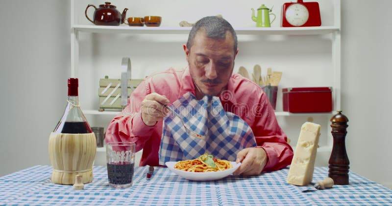 Hombre comiendo pasta italiana con salsa de tomate en casa. juego de mesa con un mantel a cuadros
