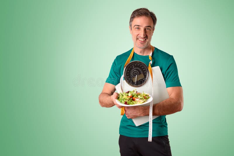 Hombre con cinta de medida de escala y ensalada en fondo verde imagen de archivo libre de regalías