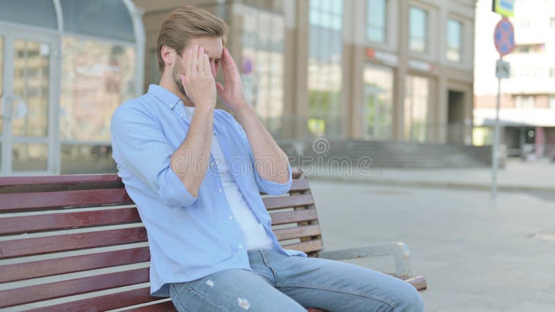 Hombre con dolor de cabeza sentado al aire libre en un banco imágenes de archivo libres de regalías